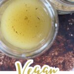 Top-down view of a jar filled with light yellow vegan chicken stock, with another jar of dried ingredients nearby. Text at the bottom reads "Vegan Chicken Stock"—a perfect vegan chicken broth recipe for all your soups and stews.