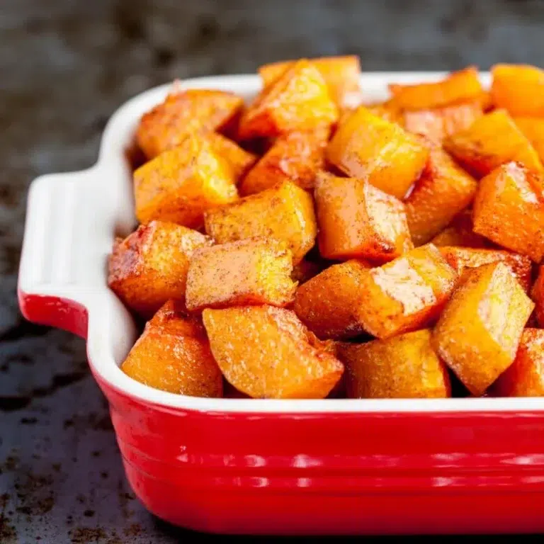 Family-Pleasing Easy Vegan Thanksgiving Recipes 7 Cubed roasted butternut squash with a golden-brown exterior in a red and white ceramic baking dish.
