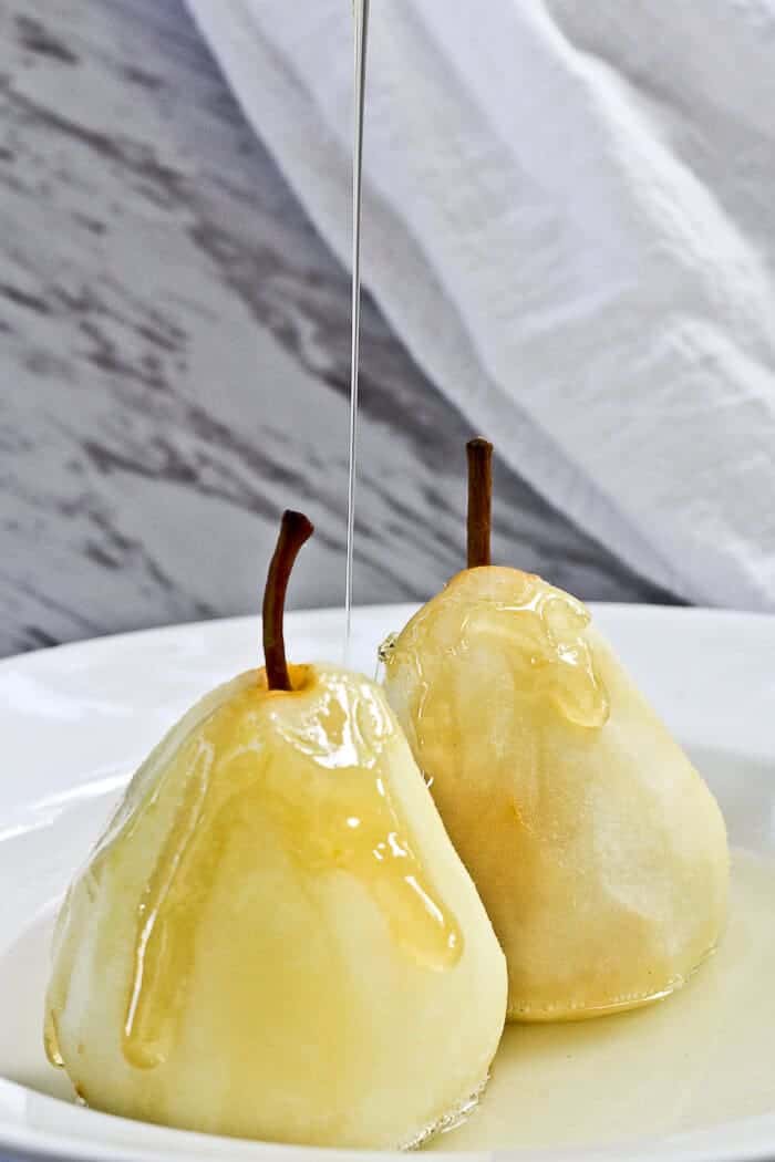 50 Delicious Vegan Desserts With Fruit That You Will Love 24 Two peeled pears are placed on a white plate while a stream of honey or syrup is being poured over them, creating one of the simplest yet elegant vegan desserts with fruit.