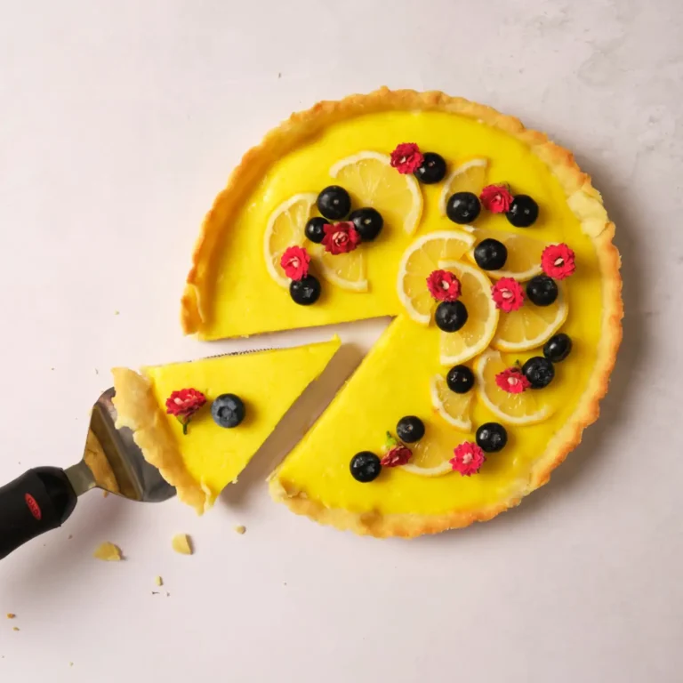 50 Delicious Vegan Desserts With Fruit That You Will Love 32 A lemon tart topped with lemon slices, blueberries, and red berries-one slice being lifted with a pie server. This is a delightful example of vegan desserts with fruit.
