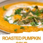 A bowl of creamy vegan roasted pumpkin soup topped with pumpkin seeds, fresh herbs, and a swirl of cream.