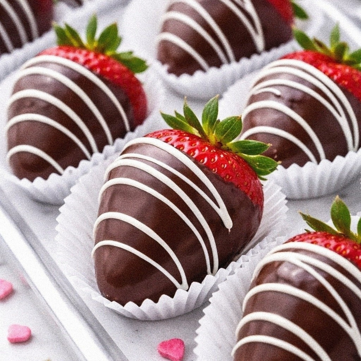 Chocolate-covered strawberries made with vegan chocolate and finished with a white chocolate drizzle, arranged in white paper cases on a tray—an elegant vegan dessert for any occasion.