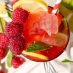 A glass of Raspberry Mojito Mocktail with ice, lemon slices, fresh raspberries, and mint, garnished with a striped straw. This non-alcoholic drink is refreshing and perfect for summer. Text at the bottom reads "Raspberry Mojito Mocktail.