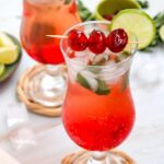 Two glasses of Shirley Temple Mocktail with ice, lime slices, and maraschino cherries on coasters—an irresistible Valentine’s Drink to enjoy. Each glass is labelled "Shirley Temple Mocktail Recipe.