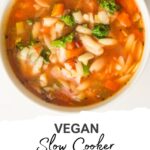 A bowl of Vegan Minestrone Soup with orzo, beans, carrots, kale, and tomato broth, viewed from above. Text reads: Vegan Slow Cooker Minestrone Soup—perfect for your slow cooker cooking.