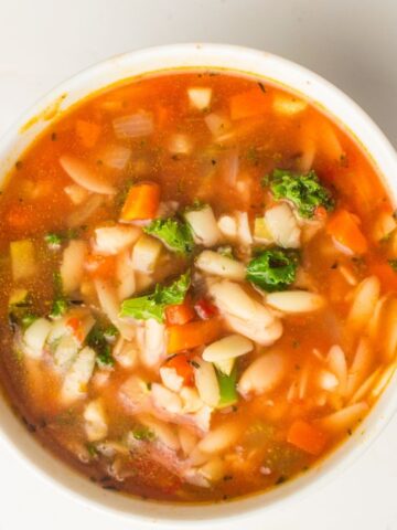 A bowl of vegan minestrone soup with pasta, beans, carrots, tomatoes, broccoli, and leafy greens simmered in a tomato-based broth—perfectly cooked in a slow cooker for rich flavour.