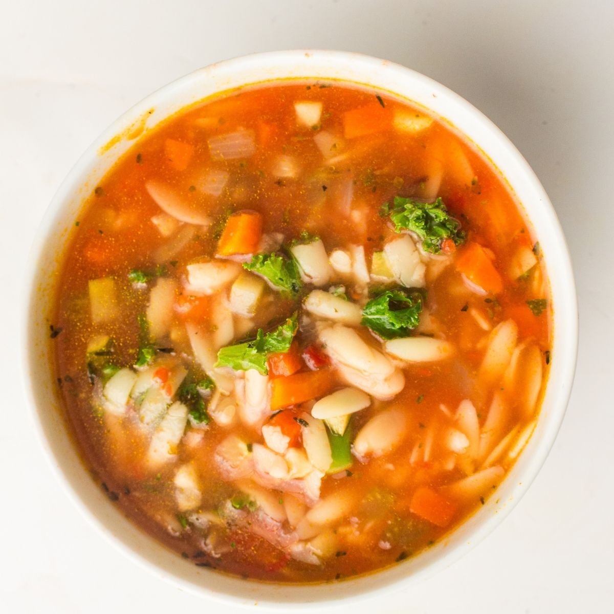 A bowl of vegan minestrone soup with pasta, beans, carrots, tomatoes, broccoli, and leafy greens simmered in a tomato-based broth—perfectly cooked in a slow cooker for rich flavour.