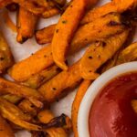 Close-up of crispy air fryer sweet potato chips, made from frozen, beside a small bowl of tomato ketchup. Text overlay reads "How To Cook Sweet Potato Chips In An Air Fryer.