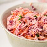 A close-up of a bowl of creamy vegan coleslaw with shredded carrots, cabbage, and parsley—a perfect vegan coleslaw recipe for any occasion.
