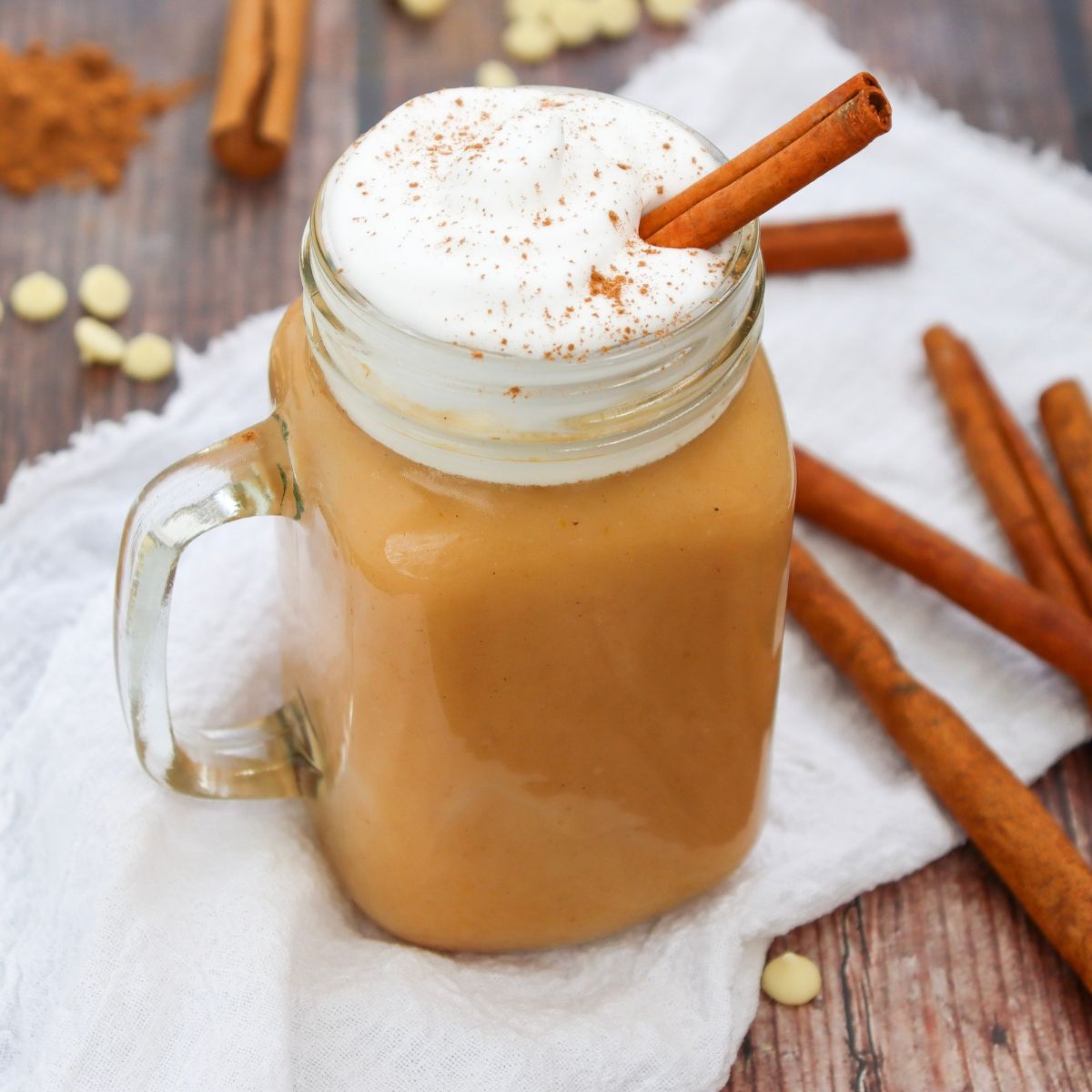 A jam jar filled with a beige drink, topped with whipped cream and a cinnamon stick.